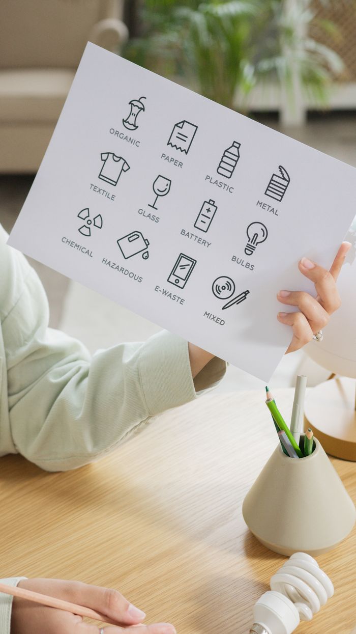 Services Close-up of a person holding a paper with recycling symbols above a wooden table.